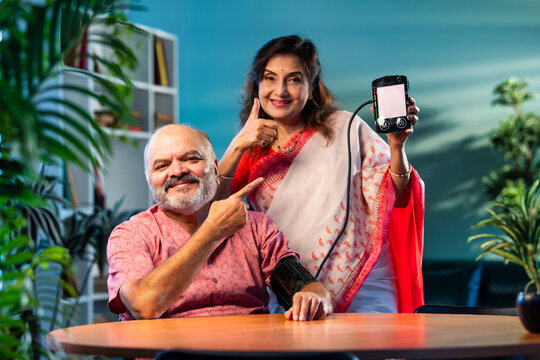 Indian senior couple using BP monitor at home, pleased with normal blood pressure reading