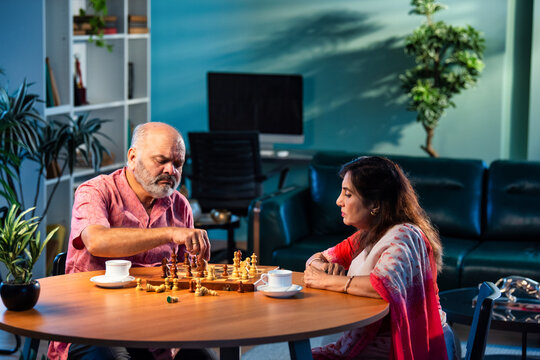 Indian senior couple playing chess game at home, engaged in fun strategy and bonding time