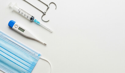 Medical tools including a syringe, thermometer, face mask, and forceps arranged on a white surface.