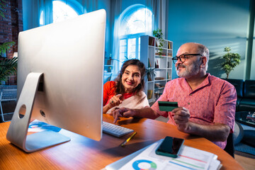 Elderly Indian couple making online payment using credit card and laptop at home
