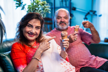 Old Indian couple eating ice cream sitting together and enjoying sweet moment indoors