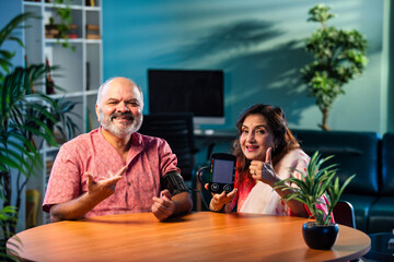 Indian senior couple using BP monitor at home, pleased with normal blood pressure reading