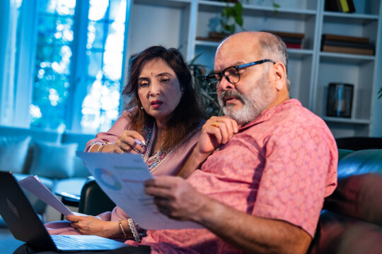 Senior Indian couple working on monthly finances together using laptop and documents at home