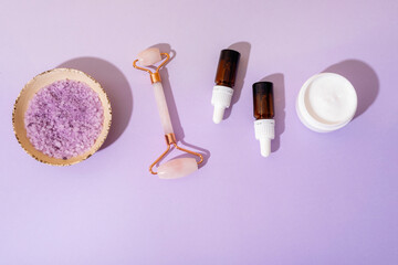 Spa cosmetic set with cream jar, essential oil bottles, rose quartz face roller and sea salt on...