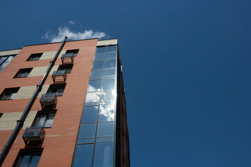 The glass facade of the red brick building reflects the blue sky with white clouds.