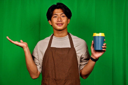 Young Man Wearing Apron Holding Coffee Cup Standing in Green Screen Studio - Powered by Adobe