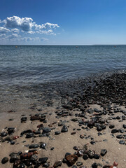 Close-up of wet pebbles scattered on a sandy beach in Odesa, Ukraine, with gentle sea waves sparkling in the background. The sunlit stones create a natural texture and coastal atmosphere, perfect for
