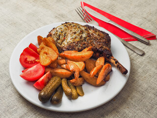 A plate of food with a premium pork chop in the bone, wedges potatoes, and tomatoes. The plate is...