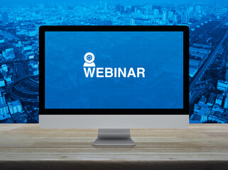 Webinar flat icon on desktop modern computer monitor screen on wooden table over city tower,...