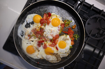 Four fried eggs sizzling in a pan, surrounded by vibrant chopped tomatoes, colorful peppers, and...