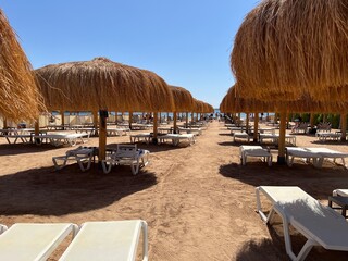 Sun loungers under thatched beach umbrellas on the beach overlooking the sea coast and blue sky