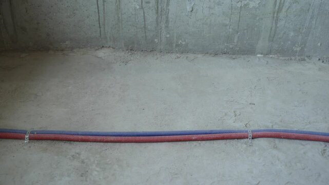 Red and blue corrugated plastic electrical conduits are being installed on a concrete floor in a building under construction