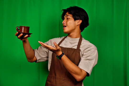 Young Man Wearing Apron Holding Coffee Cup and Saucer in Front of Green Screen