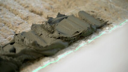 Construction worker spreading cement on the floor, using a laser level for precise application