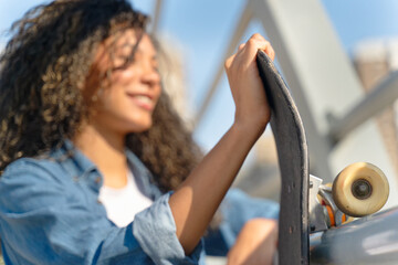 Smiling young woman holding her skateboard on a bridge in the city