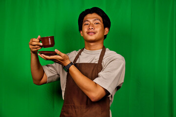 Young Man Wearing Apron Holding Coffee Cup in Front of Green Screen