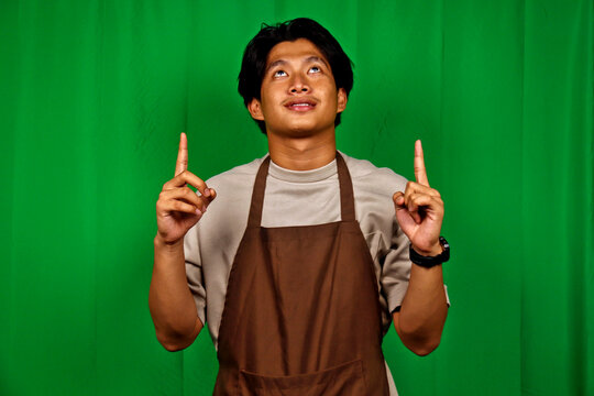 Young Man Wearing Apron Pointing Up in Front of Green Screen - Powered by Adobe