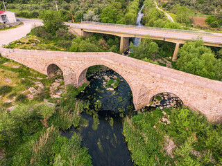 Ancient stone bridge stands majestically, arching over a river winding through a landscape of...
