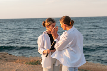 Women Beach Sunset Comforting - Two women stand on a cliff overlooking the ocean at sunset, one...