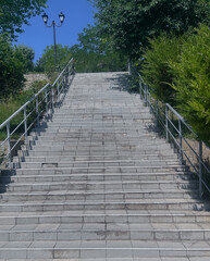 Low angle view of old concrete stairs leading upward towards a metal gate under a blue sky. Symbol of progress, success, and goal achievement.