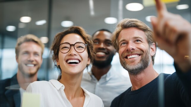 The moment of inspiration strikes as a smiling businesswoman points to a solution on a board covered in notes, her happy colleagues looking on in agreement.