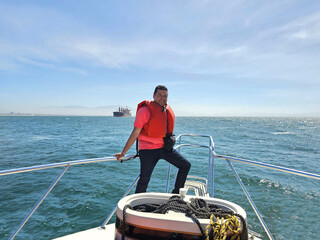 Fototapeta premium Dark-skinned Latino adult man wearing a life jacket enjoys a boat tour with ocean views during his vacation
