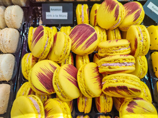 Colorful yellow macarons with vibrant red streaks are displayed together in a French pastry shop