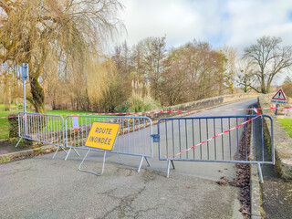 Road closure barriers with warning sign in French indicating flooded route, surrounded by trees and...
