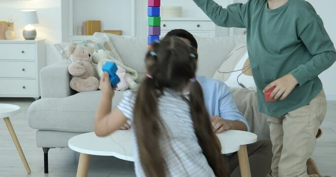 Children and their father building tower with colorful cubes at white table indoors