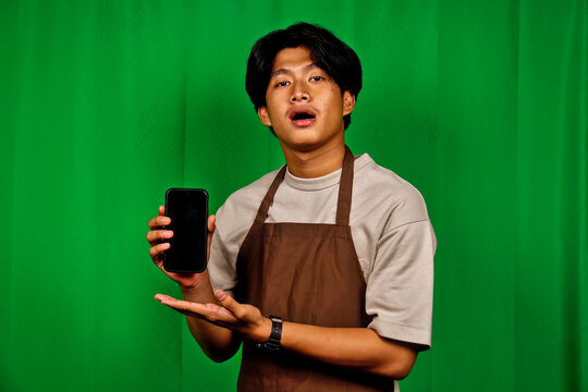Young Man Wearing Apron Holding Smartphone in Front of Green Screen