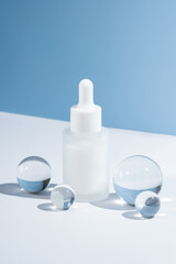 Mockup of glass dropper bottle with face serum or essential oil on blue background with glass balls. The concept of beauty cosmetics, natural products for moisturizing and restoring the skin.