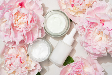 Skincare duo with pink peonies: glass serum bottle and cream jar. Feminine, elegant product shot...