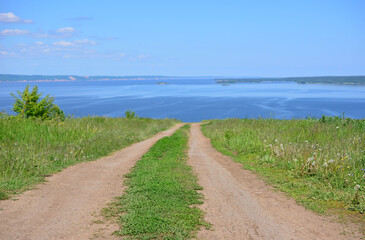 A dirt road leads to a river view from a grassy hill under a bright blue sky copy space 