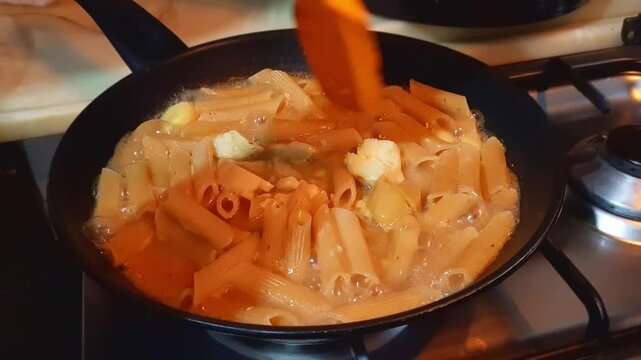 Cooking Stirring Creamy Penne Pasta Mixed Soup Broth Curry Golden Yellow Cheese Potato Italian Boiling Bubbling Steam Teflon Nonstick Pan Gas Stove Kitchen Dark Dramatic Food Recipe European Delicious