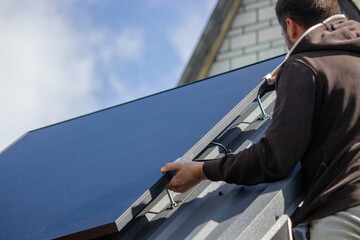 A man is installing solar panels on a roof. Selective focus
