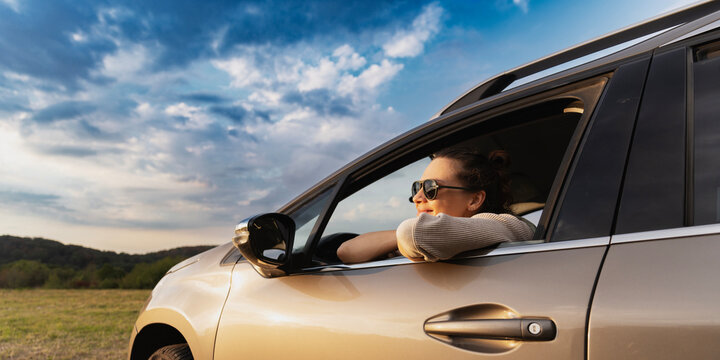 Happy young woman drivier looking out of car window, auto travel and adventure