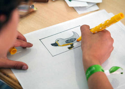 Konzept Basteln und Kreativit&auml;t Kinder: Detailblick von oben auf die Hand eines farbigen Jungen der mit einem Buntstift ein fantasievolles Tierbild ausmalt, weitere Materien auf dem Tisch, Copy Space