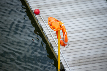 An orange lifebuoy and rescue float mounted on a yellow pole by a wooden dock.