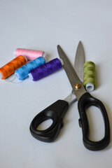 colorful sewing supplies including spools of thread, tailor’s chalk, and scissors arranged on a...