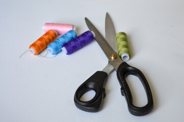 colorful sewing supplies including spools of thread, tailor’s chalk, and scissors arranged on a...
