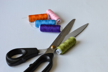 colorful sewing supplies including spools of thread, tailor’s chalk, and scissors arranged on a...