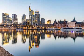 View over the River Main with a modern illuminated skyline in the background in the evening, at...