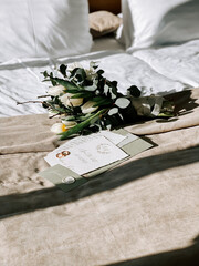 Bridal bouquet and wedding invitation on an elegantly made bed in a cozy room