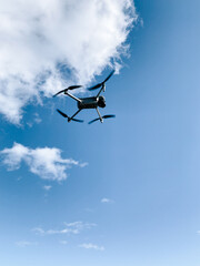 Drone flying against a clear blue sky with fluffy white clouds in a sunny location
