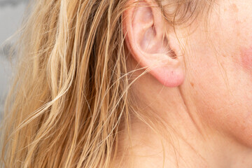 Detailed macro shot of an adult woman's ear with blonde hair, showing skin and texture in daylight....