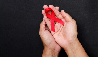 AID red ribbon in hand on a black background, a symbol of the fight against HIV, AIDS and cancer. concept of helping those in need.