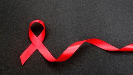 AID red ribbon in hand on a black background, a symbol of the fight against HIV, AIDS and cancer. concept of helping those in need.