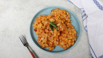 Perkedel Jagung or Bakwan Jagung, corn fritters is Indonesian traditional food. Savory snack made of corn, egg, flour, spring onion, pepper and salt. Served in blue plate on grey background