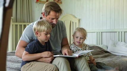 Happy father reading book to his curious children indoor. Closeup. Daddy, daughter and son spending time together. Family time comes in various forms. Dad read story to small kids. Authentic Lifestyle - Powered by Adobe