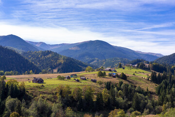 Obraz premium Breathtaking Scenic View of the Ukrainian Carpathians Capturing a Serene Village Surrounded by Lush Green Hills and Colorful Autumn Foliage Under a Clear Blue Sky